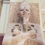 Egyptian statue with hieroglyphics behind and white pillar